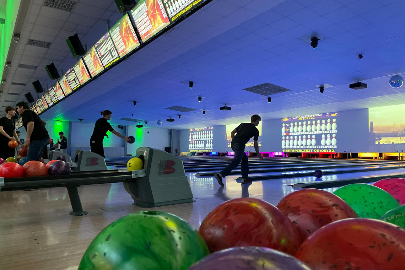 Zwei Personen die je eine Bowlingkugel werfen und zwei die dahinter stehen.