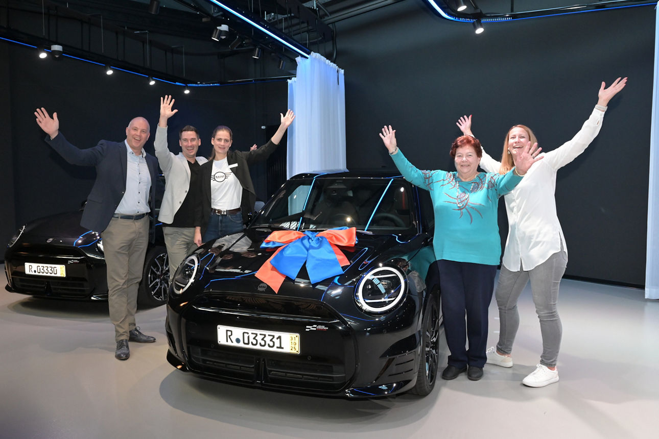 In einem Showroom freut sich die Gewinnerin neben ihrem MINI Cooper SE