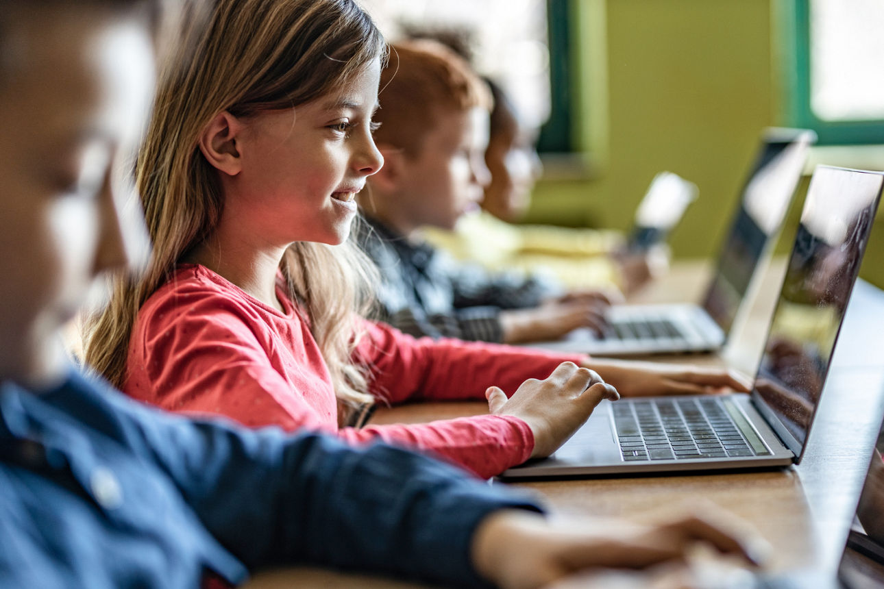 Mehrere Kinder sitzen im Klassenraum nebeneinander und arbeiten konzentriert an Laptops