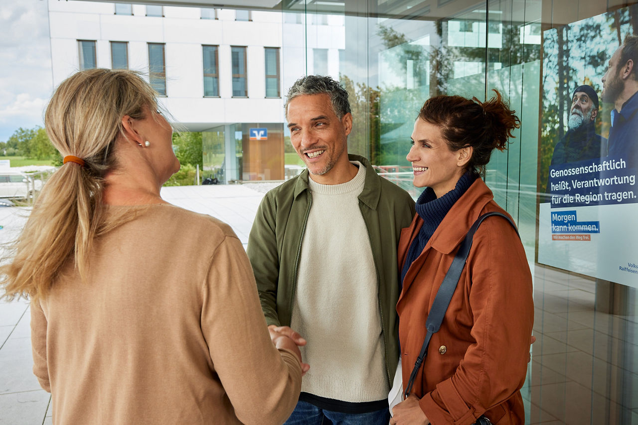 Bankberaterin steht mit einem Mann und einer Frau vor einer Volksbank-Filiale