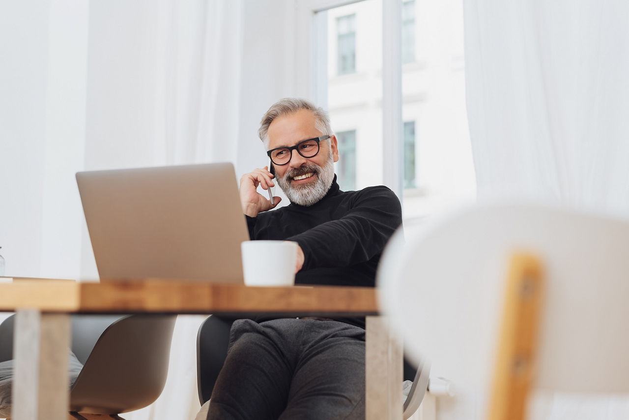 Mann lacht beim Telefonieren während er auf seinen Laptop schaut