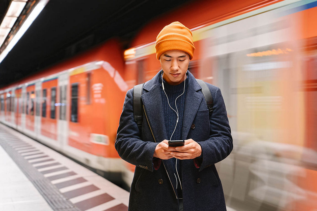 Mann in einer U-Bahn-Station, der auf sein Smartphone schaut