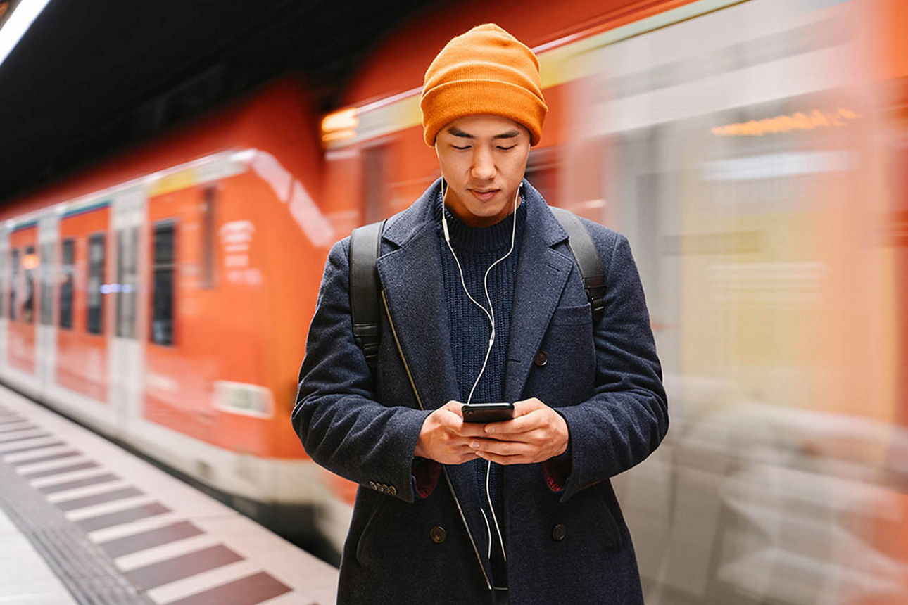 Mann in einer U-Bahn-Station, der auf sein Smartphone schaut