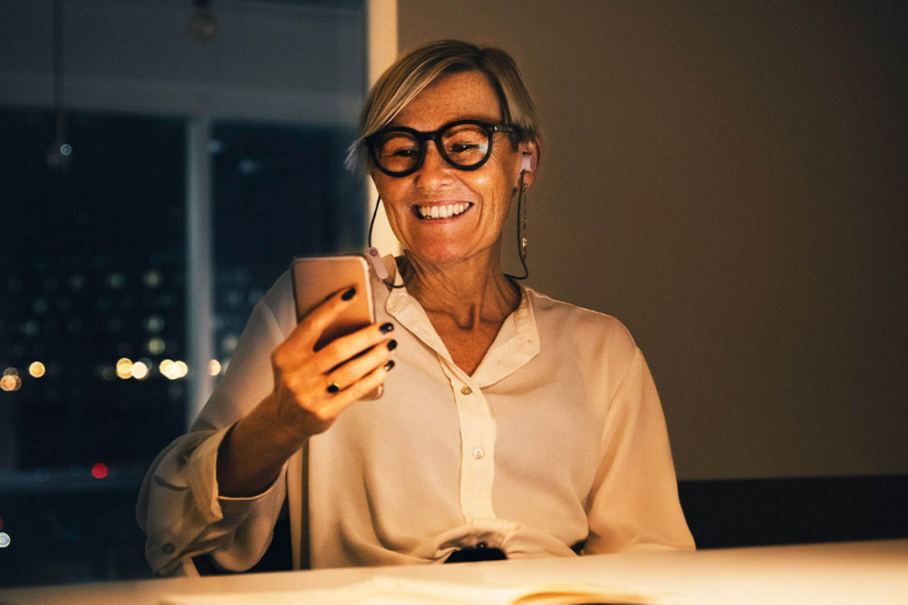 Eine Geschäftsfrau schaut lächelnd auf ihr Smartphone