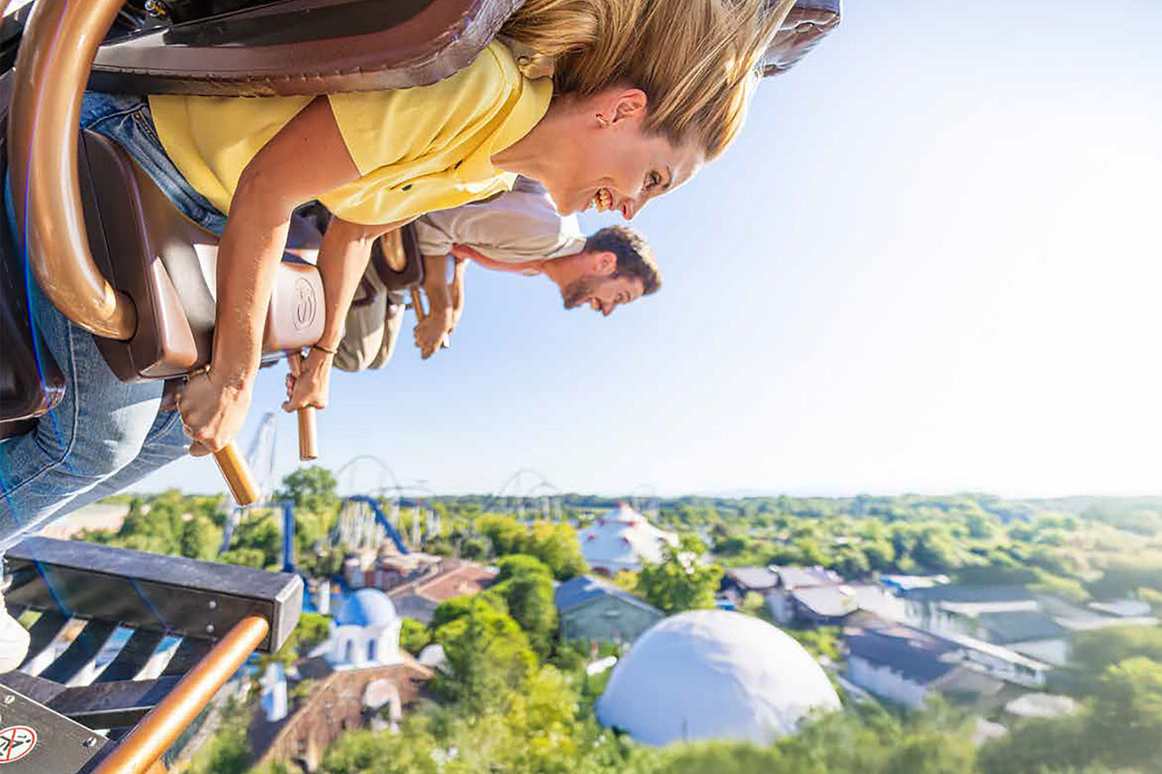 Paar in einer Achterbahn im Vordergrund und einer Europaparkkulisse im Hintergrund.