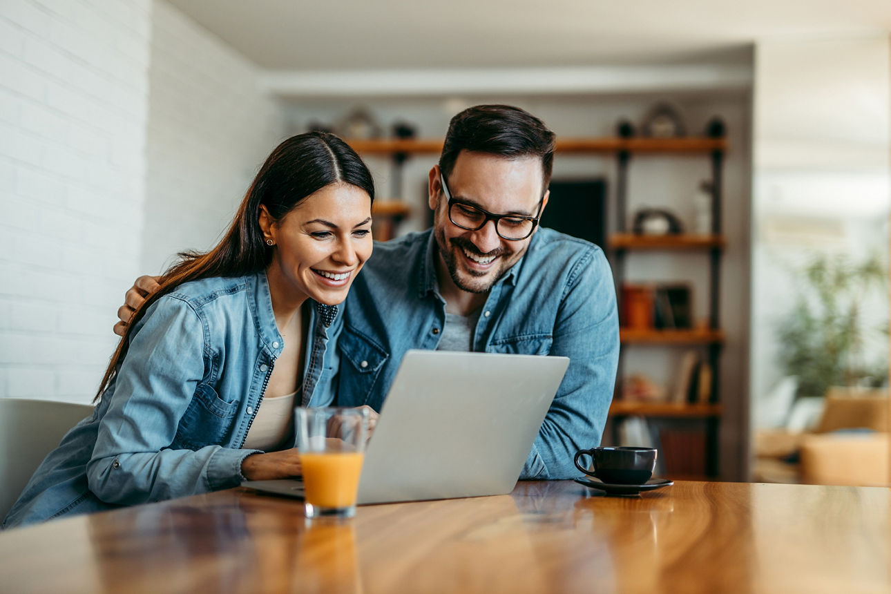 Mann und Frau sitzen am Tisch und schauen in ein Laptop