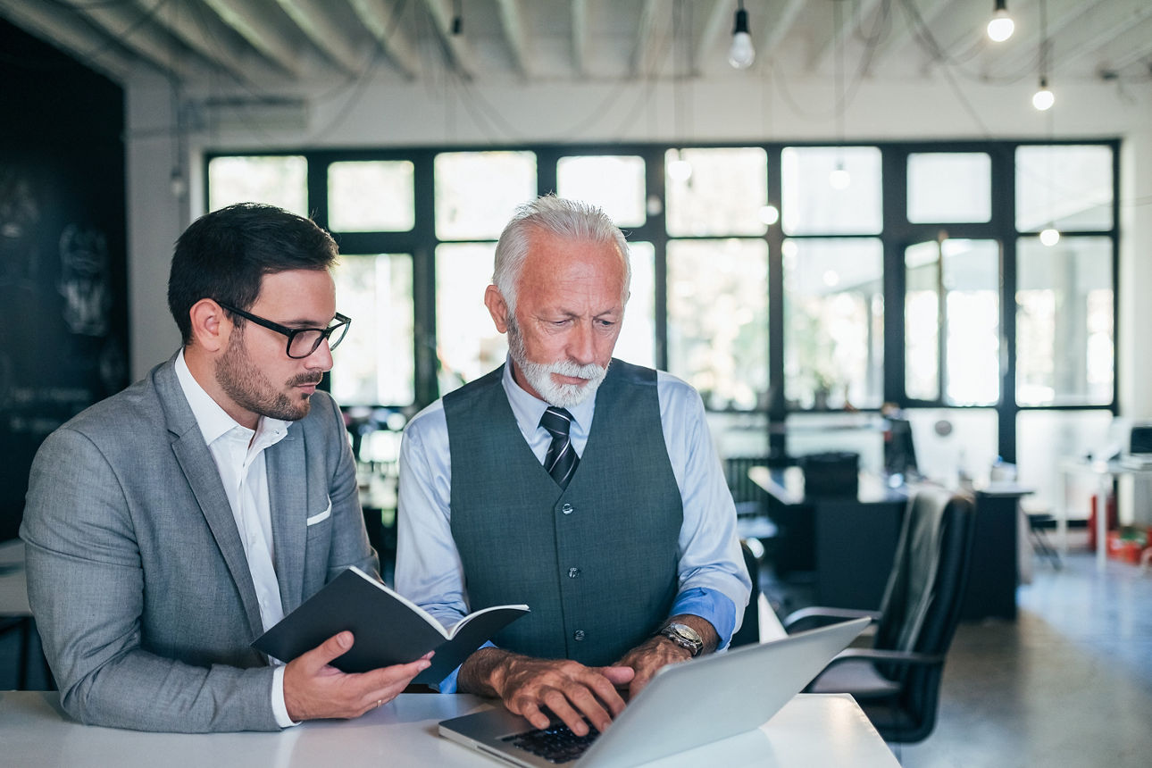 Zwei Männer stehen am Tisch und sehen sich etwas an einem Laptop an