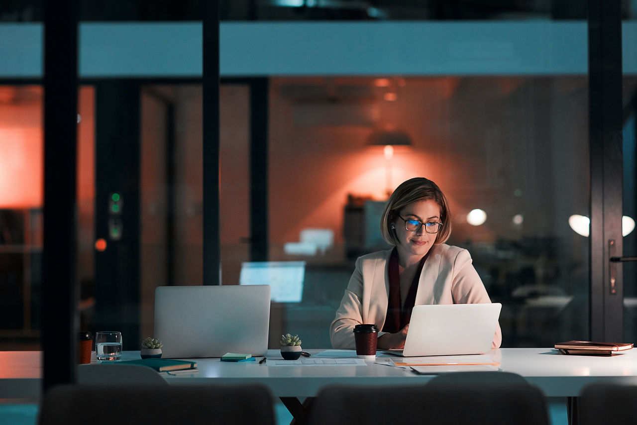 Eine Frau sitzt in einem etwas abgedunkelten Raum mit großer Fensterfront vor einem Laptop