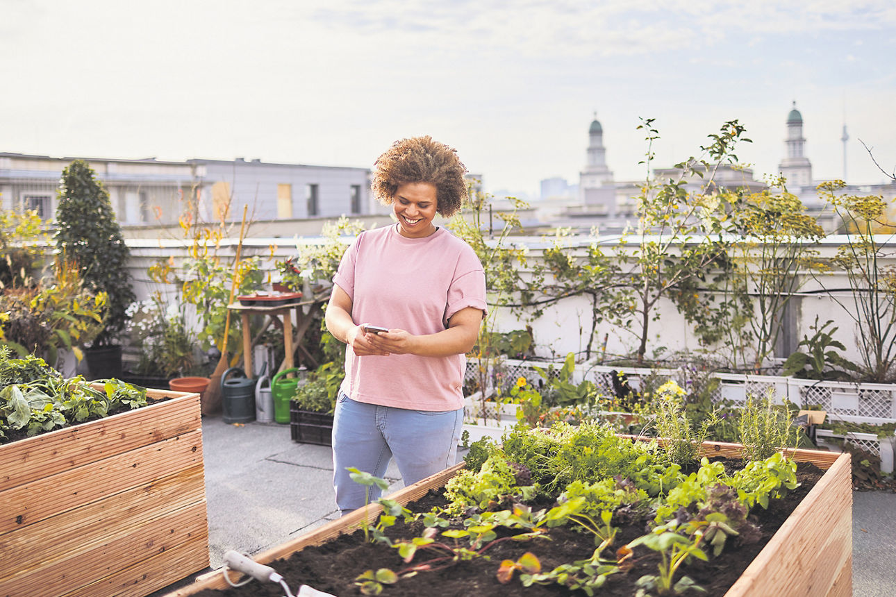 Frau steht mit einem Handy in der Hand auf einer Dachterrasse