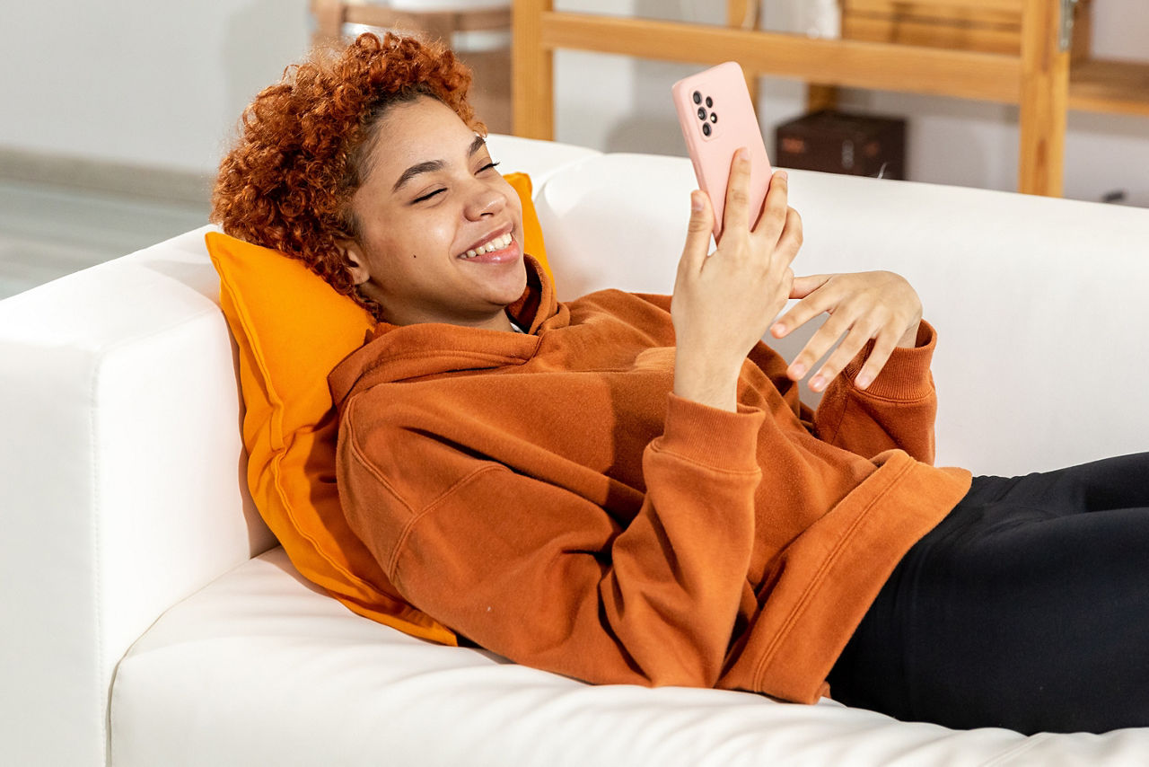 Junge Person liegt mit Handy auf einem Sofa