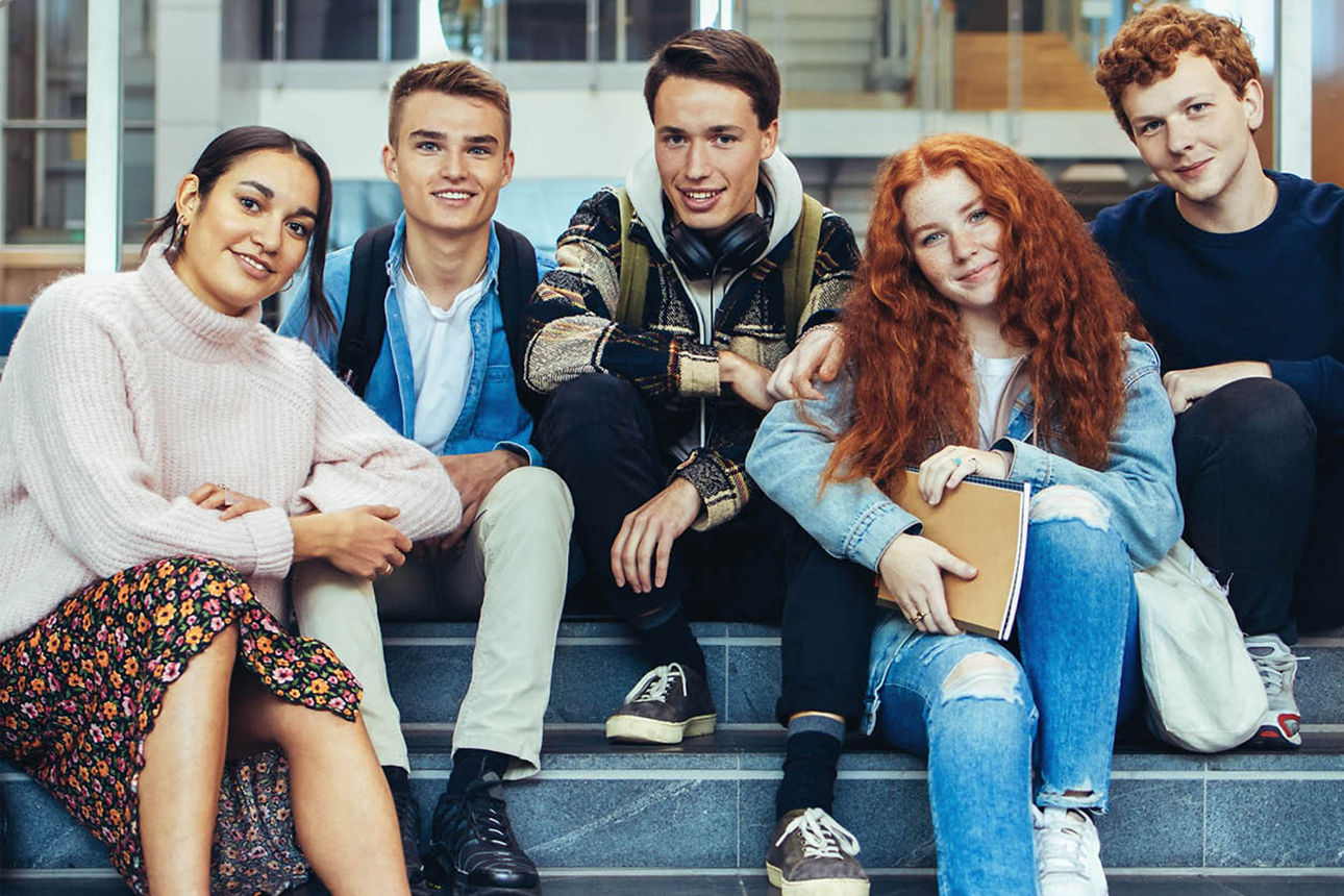 Schülergruppe bestehend aus fünf Personen sitzt auf einer Treppe