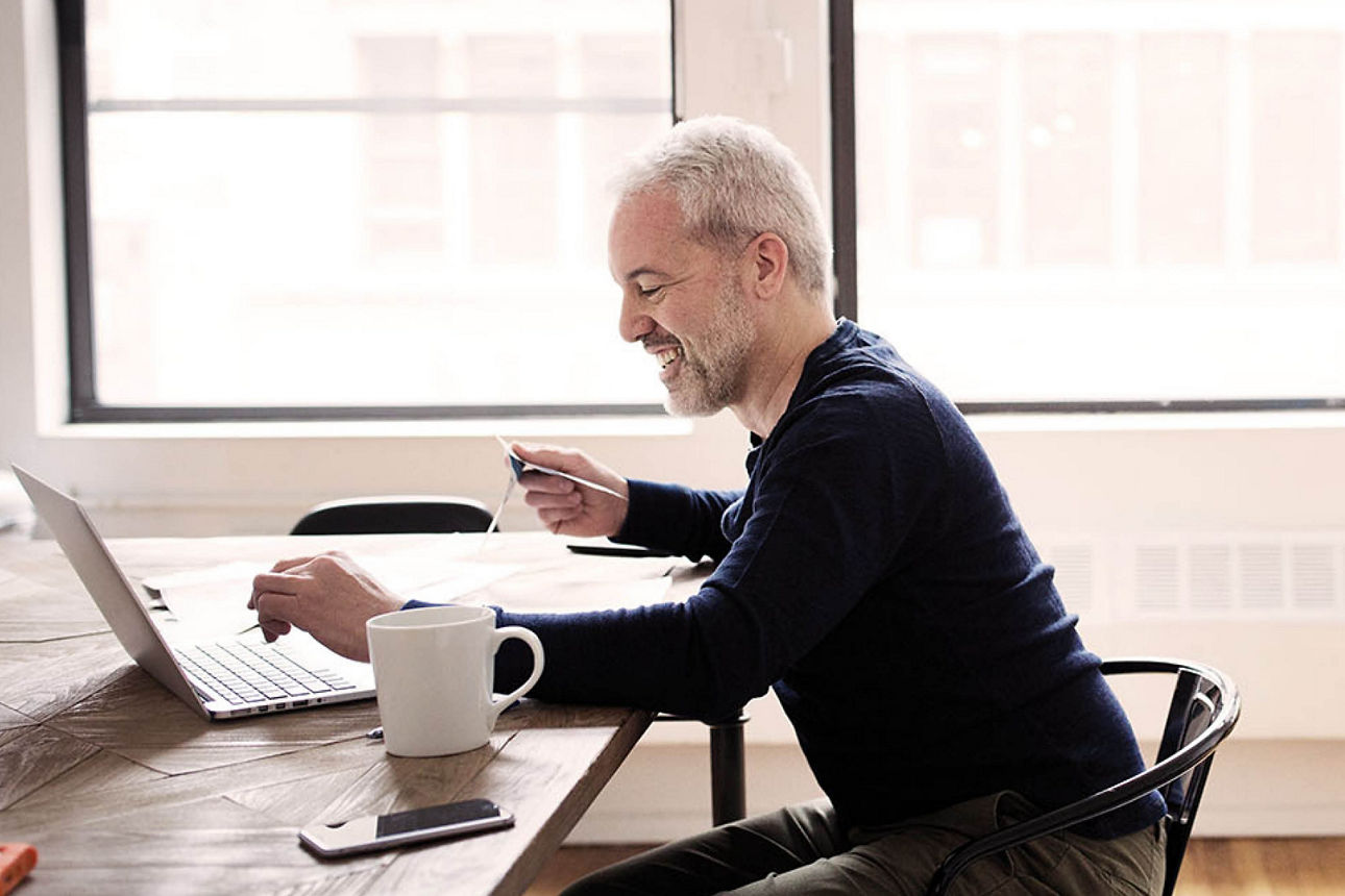 Mann sitzt mit seinem Kaffee am Laptop