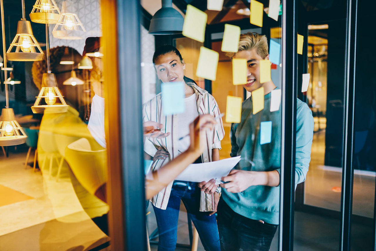Gruppe junger Personen in einer Besprechung vor Glaswand mit Haftnotizen