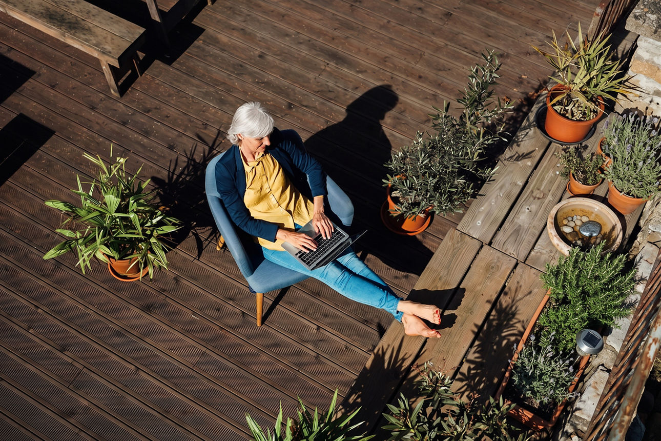 Frau sitzt mit ihrem Laptop auf einer Dachterrasse