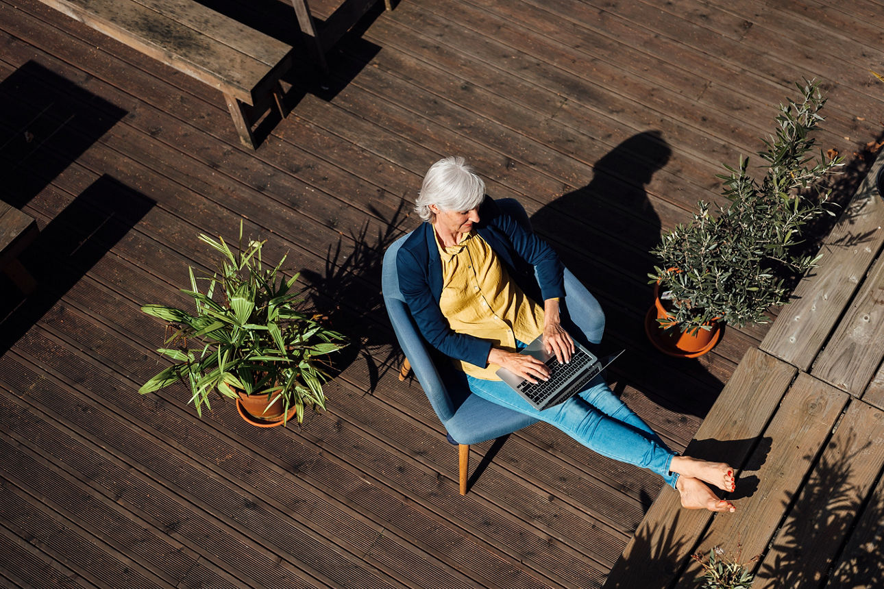 Frau sitzt mit ihrem Laptop auf einer Dachterrasse