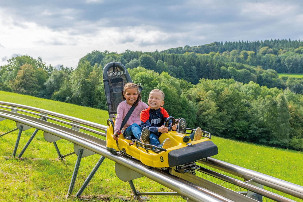 Zwei Kinder fahren mit der Sommerrodelbahn