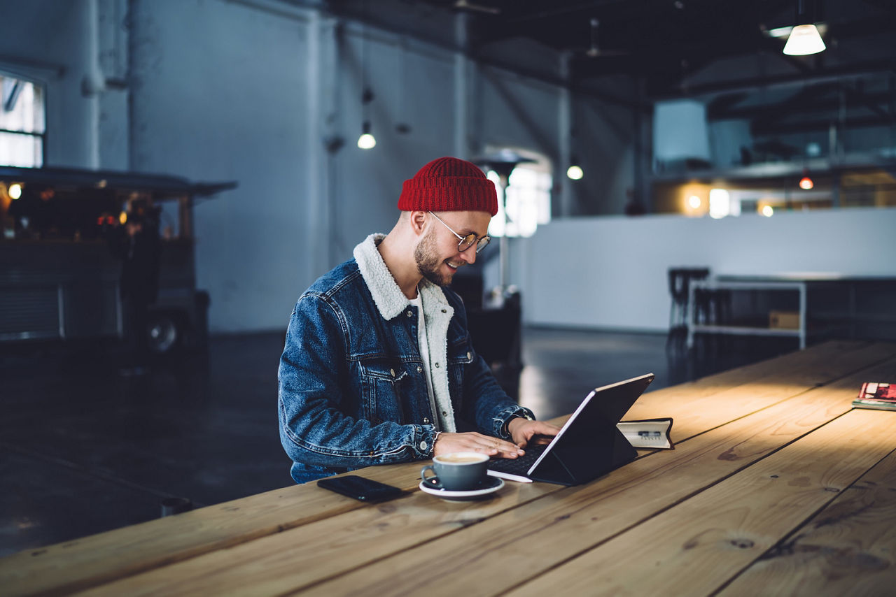 Person mit Laptop und Kaffe am langen Holztisch sitzend