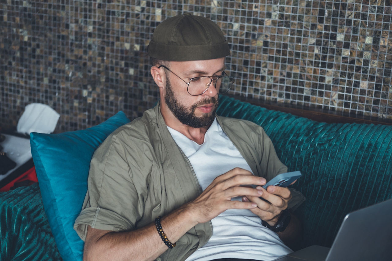 Junger Mann sitzt auf dem Sofa und sieht auf sein Handy