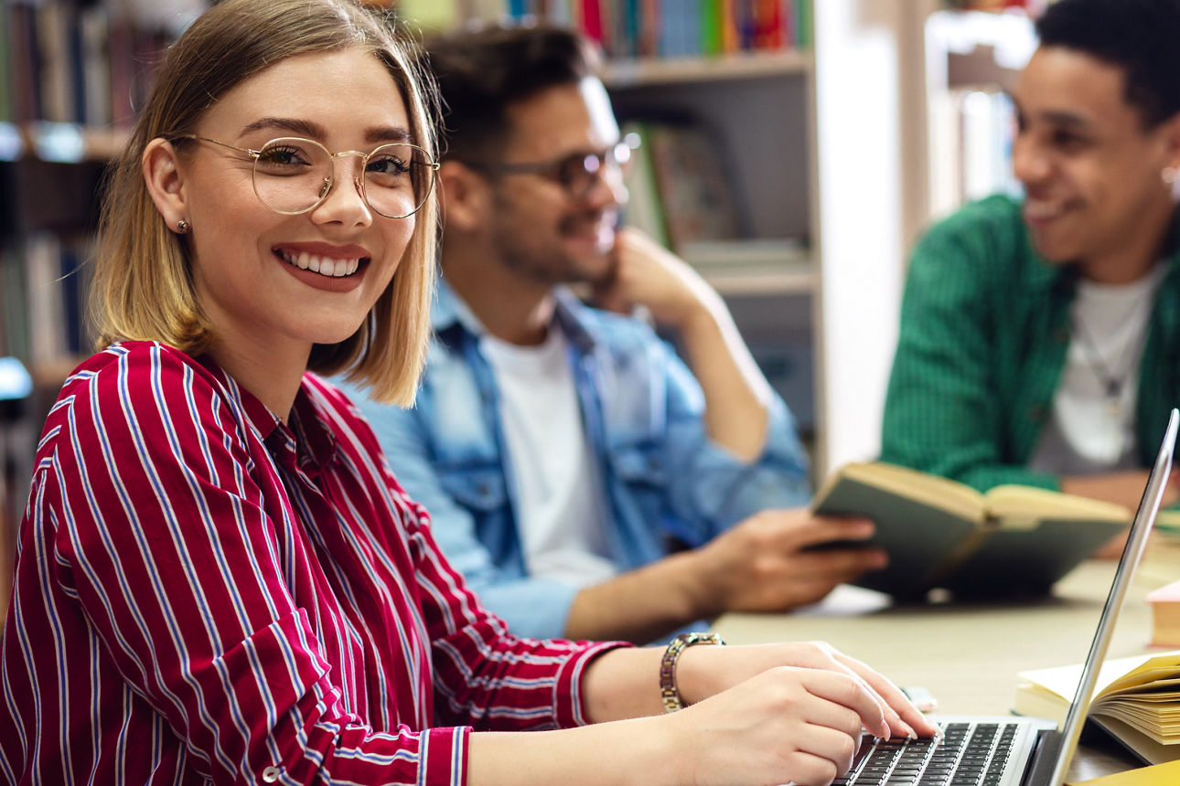 Drei Studierende sitzen in einer Bibliothek