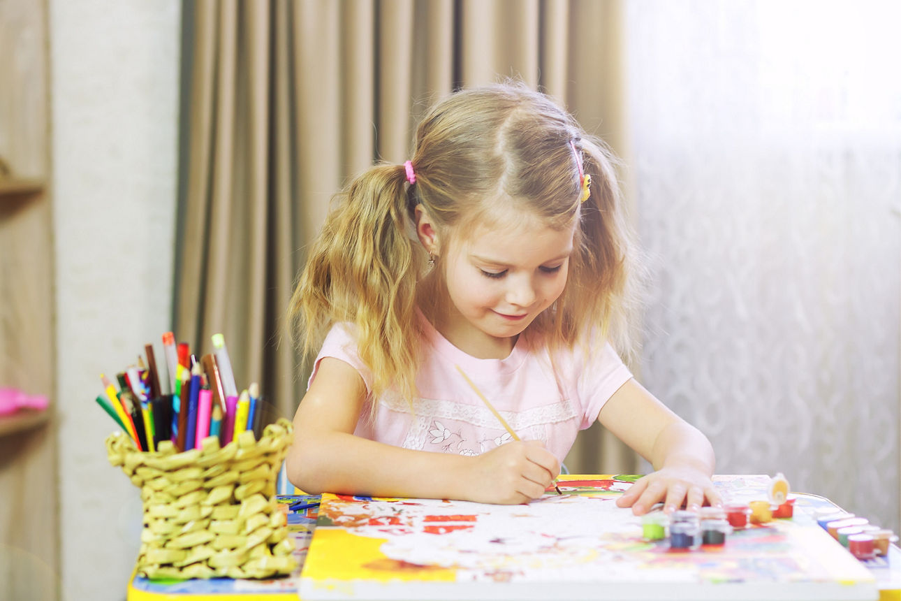 Ein kleines Mädchen sitzt an einem Tisch und hält einen Pinsel in der Hand. 