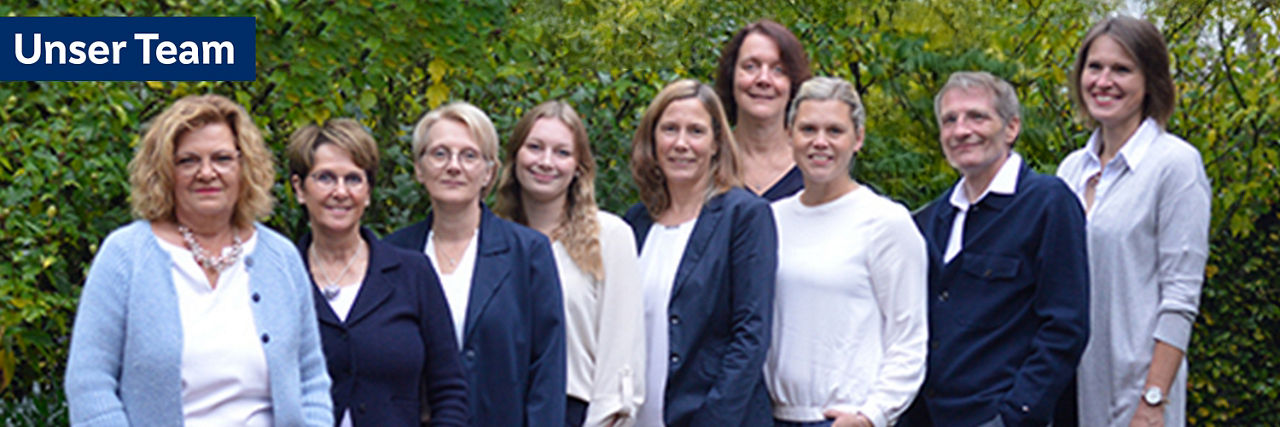 Eine Gruppe von zehn Personen steht vor einer üppigen grünen Hecke.