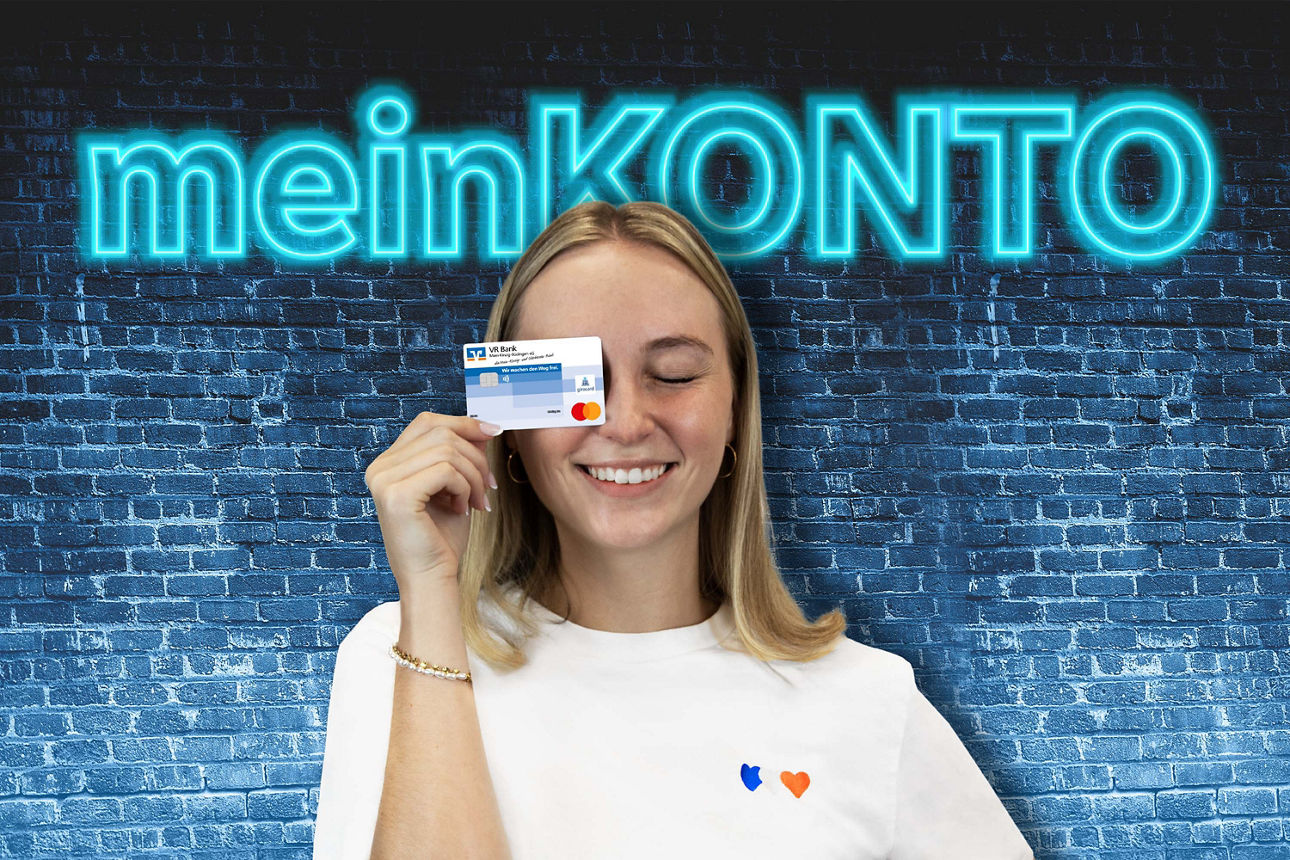 Junge Frau hält Bankkarte vor das Gesicht, im Hintergrund leuchtender Schriftzug ‚meinKONTO‘ auf blauer Ziegelwand.