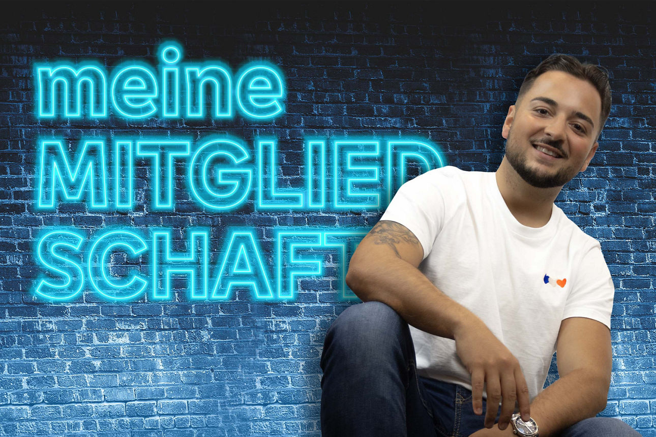 Junger Mann sitzt lächelnd vor einer blauen Ziegelwand, im Hintergrund leuchtender Schriftzug ‚meinMITGLIEDSCHAFT‘.