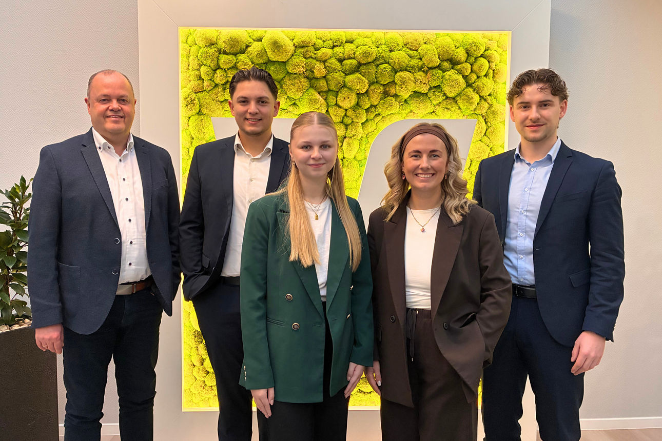 Fünf Personen in Businesskleidung stehen vor grünem Pflanzenbild, Gruppenfoto im Innenraum