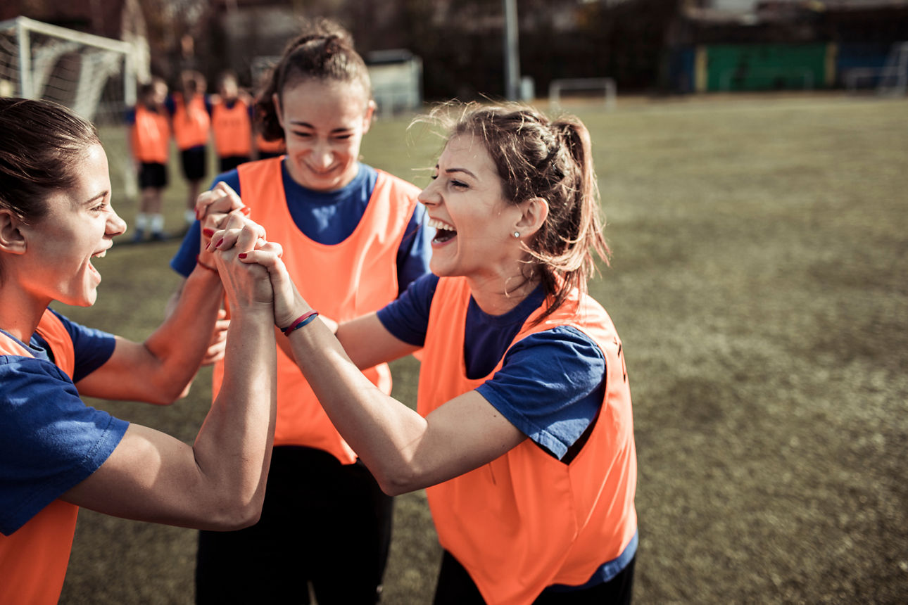 Drei Spielerinnen auf dem Spielfeld mit Trikos. 