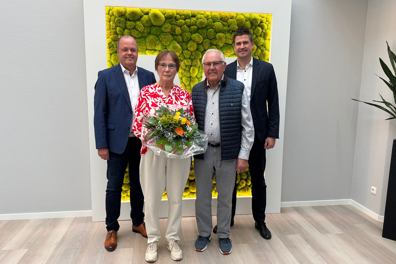 Alwin Raker mit seiner Frau und den Vorständen zum Jubiläum. Sie hält einen Blumenstrauß in der Hand.
