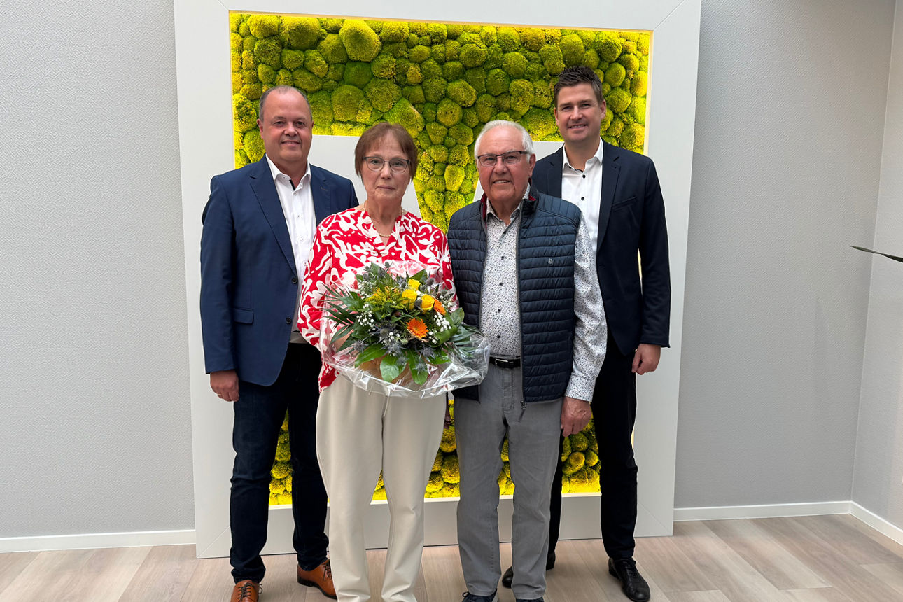 Alwin Raker mit seiner Frau und den Vorständen zum Jubiläum. Sie hält einen Blumenstrauß in der Hand.