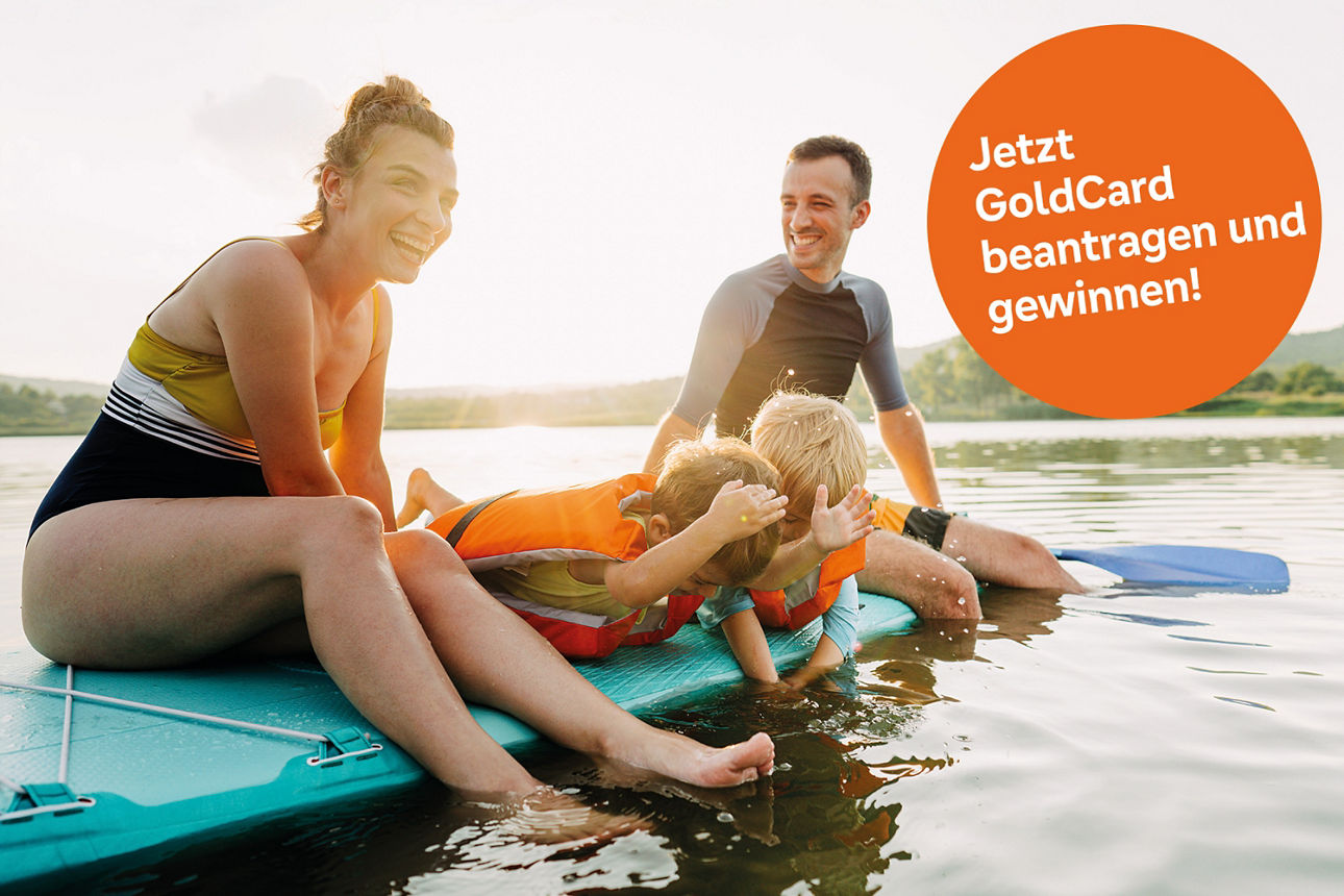 Zwei Erwachsene und zwei Kinder auf einem Stand-up-Paddle in einem See.