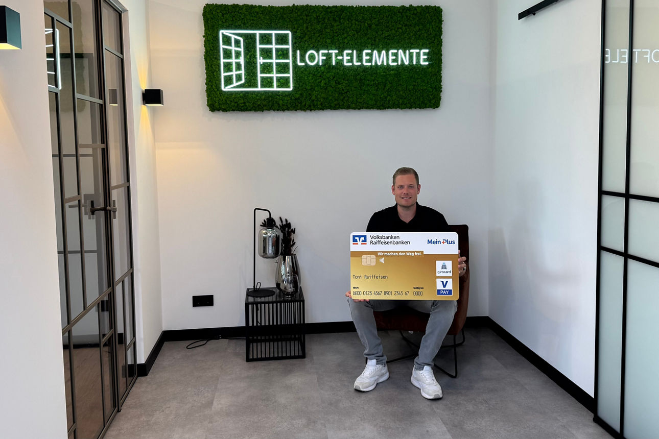 Mann präsentiert Spendenscheck im Ausstellungsraum von LOFT-ELEMENTE, gemeinsames Förderfoto im Innenbereich.