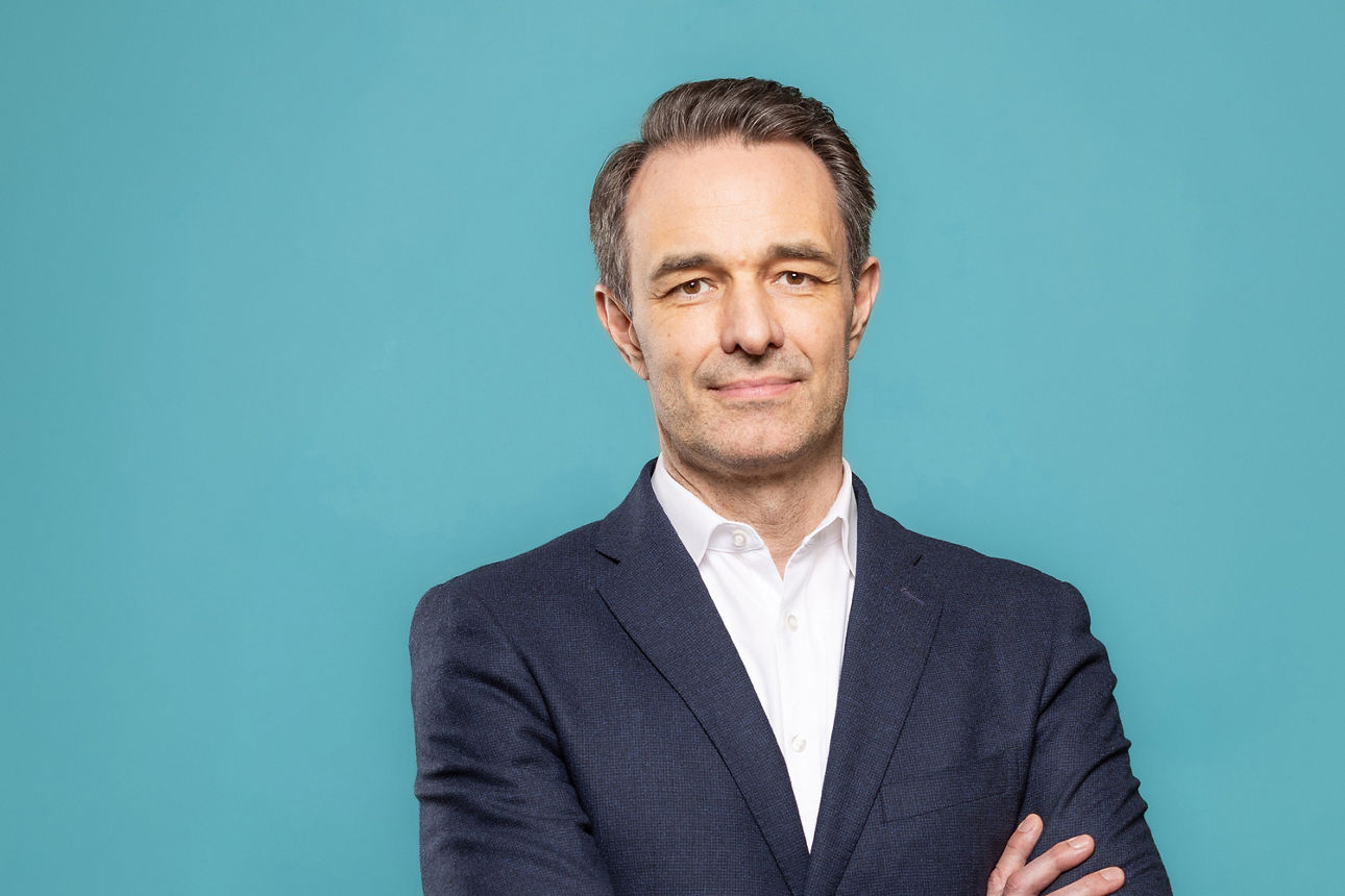 Porträt von Lars Schurich, Vorstand der VR RegionalBank, vor hellblauem Hintergrund in dunklem Anzug und weißem Hemd.