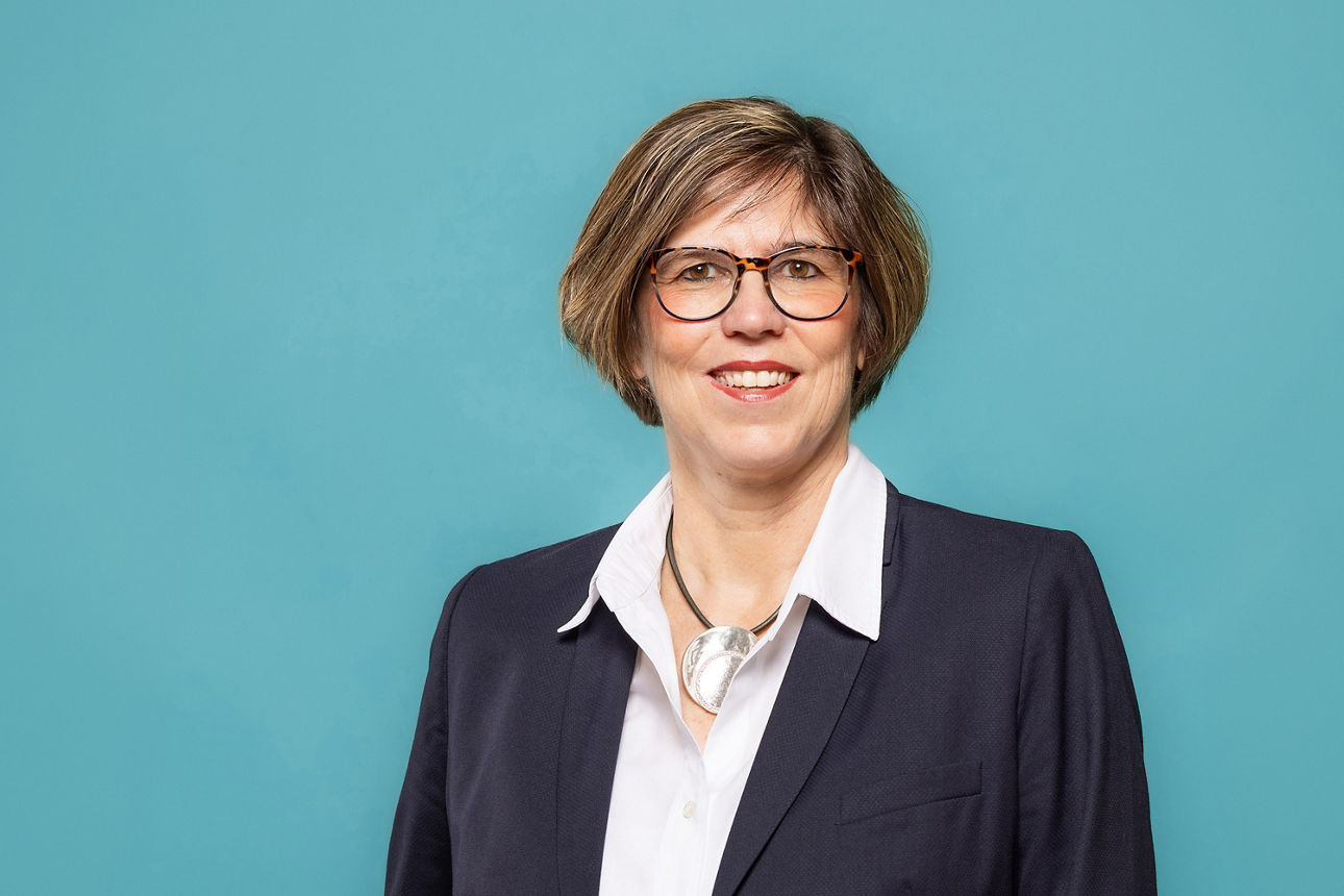 Porträt von Petra Kalbhenn, Vorstand der VR RegionalBank, vor hellblauem Hintergrund in dunklem Anzug und weißem Hemd.