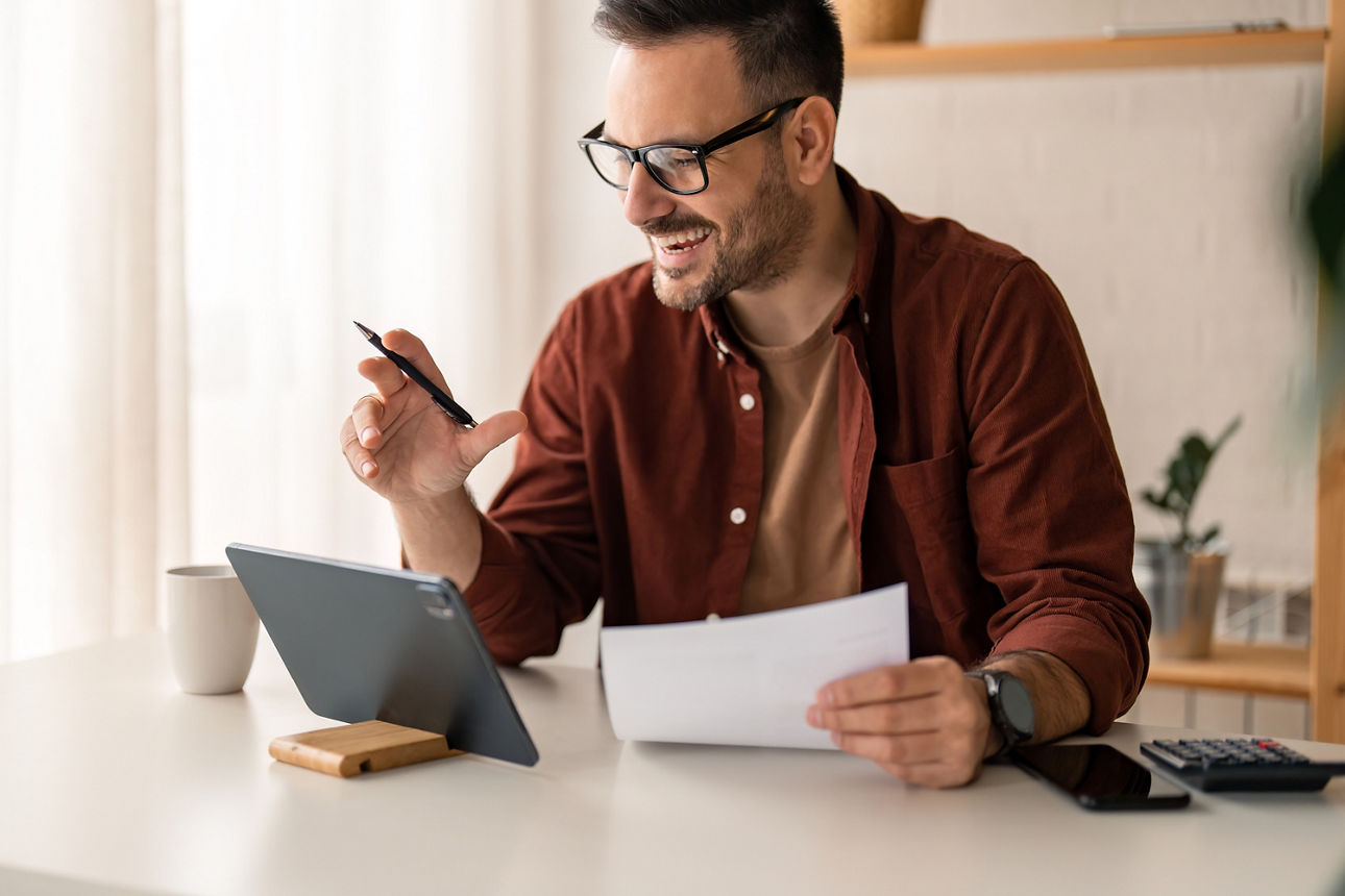 Mann sitzt am Tisch mit Tablet und hält Kugelschreiber und Zettel in der Hand