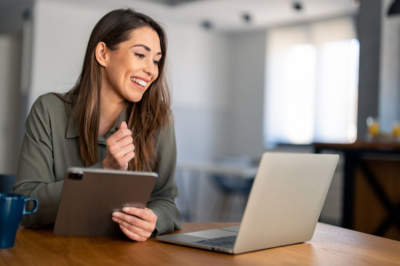 Frau sitzt am Tisch mit Laptop und Tablet in der Hand