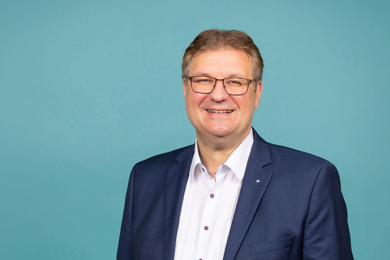 Porträt von Thomas Sälzer, Vorstand der VR RegionalBank, vor hellblauem Hintergrund in dunklem Anzug und weißem Hemd.