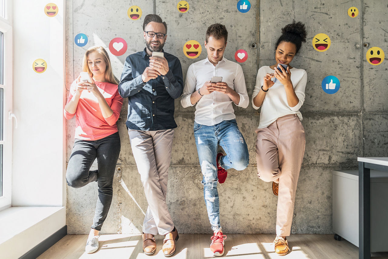 4 Personen mit Smartphones stehen an einer Wand. Um die Personen kreisen verschiedene Emojis