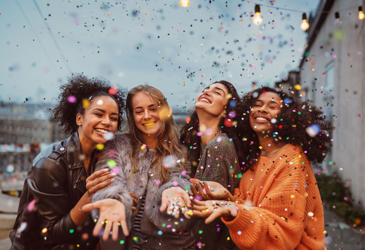Four beautiful women standing at a terrace under confetti.