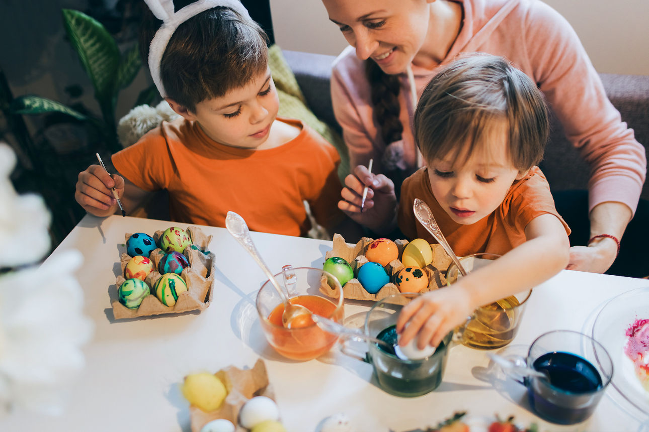 Family preparing eggs for Easter. Family with two sons wearing Bunnyâ  s Ears painting Easter eggs at home. Decorations for coloring eggs for holiday. Happy Easter concept.