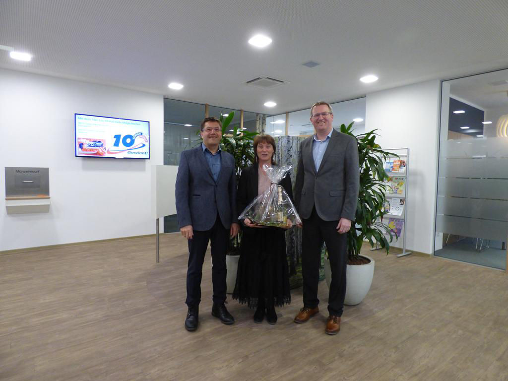 Eine Frau, die ein Geschenk in der Hand hält, posiert mit zwei Männern für die Kamera