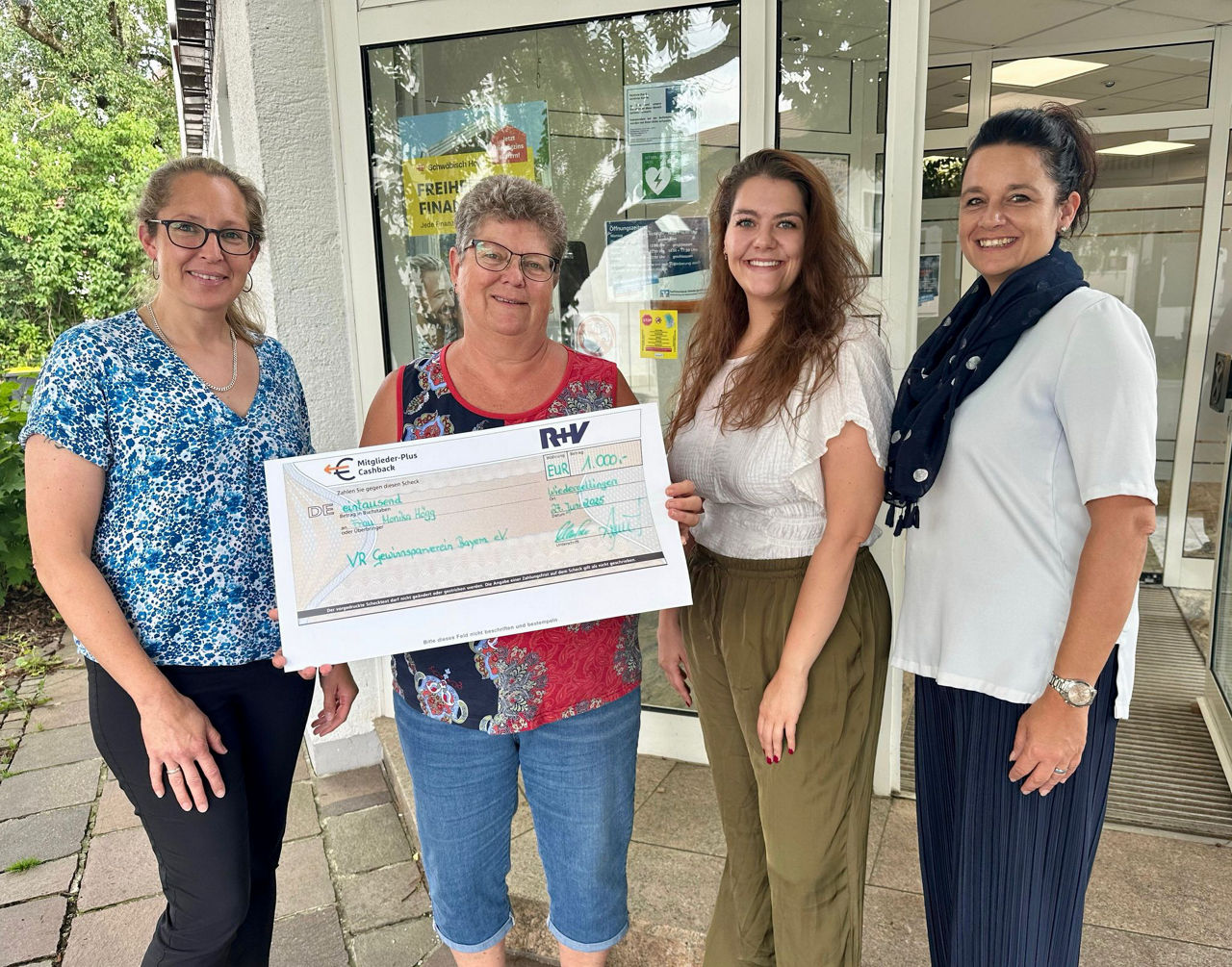 Vier Personen vor Gebäude, eine Person hält symbolischen Scheck mit ‚Gewinnsparverein‘.