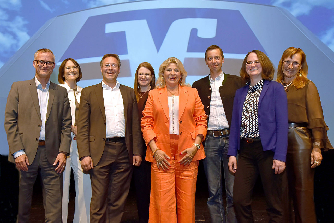 Eine Gruppe von sieben Personen steht vor einem blau-weißen Transparent.