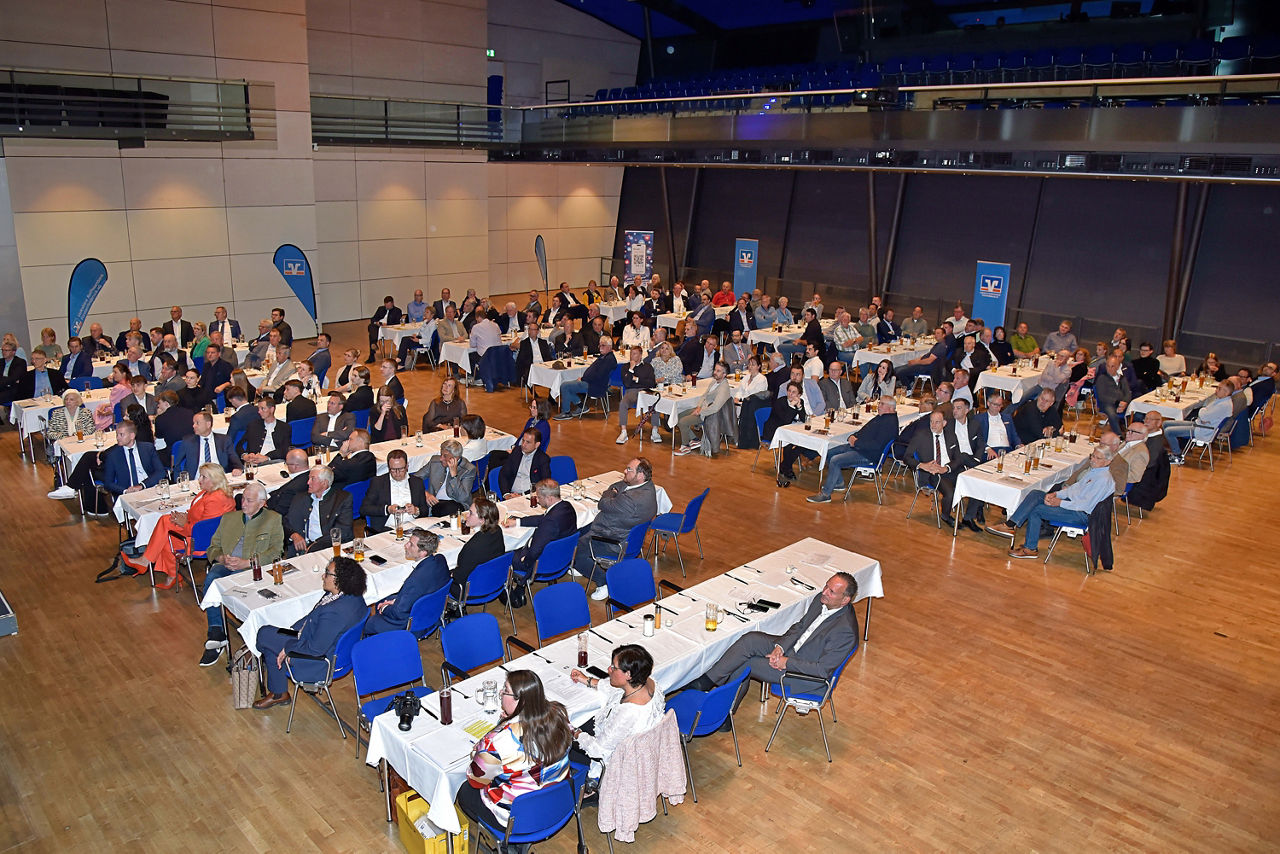 Das Bild zeigt einen großen Konferenzraum, der mit Menschen gefüllt ist.