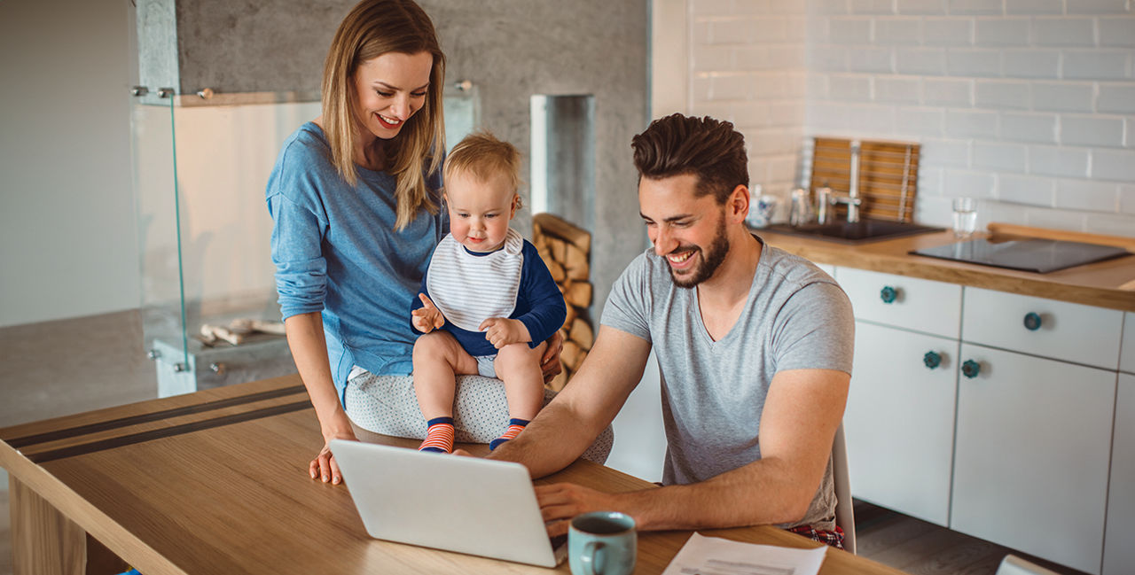 Frau und Mann mit Kind in der Küche vor einem Laptop
