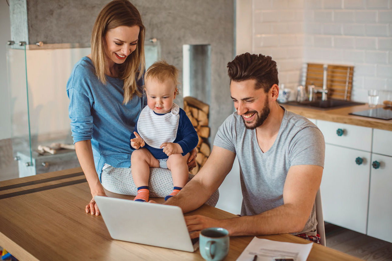 Junge Familie sitzt in Küche vor dem Laptop