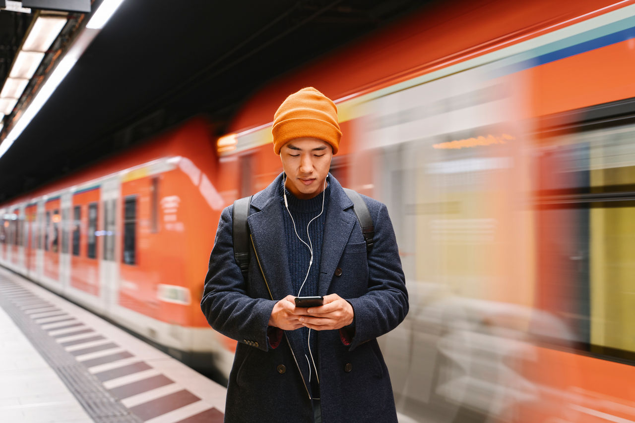 Germany, Frankfurt, Stylish man with yellow hat and earphones in metro station