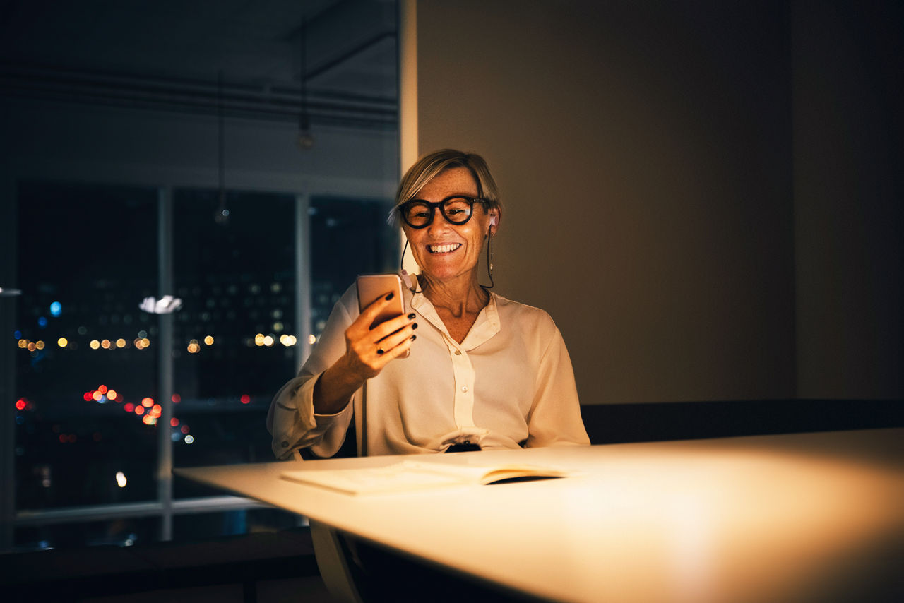 Frau am Schreibtisch checkt ihr Handy