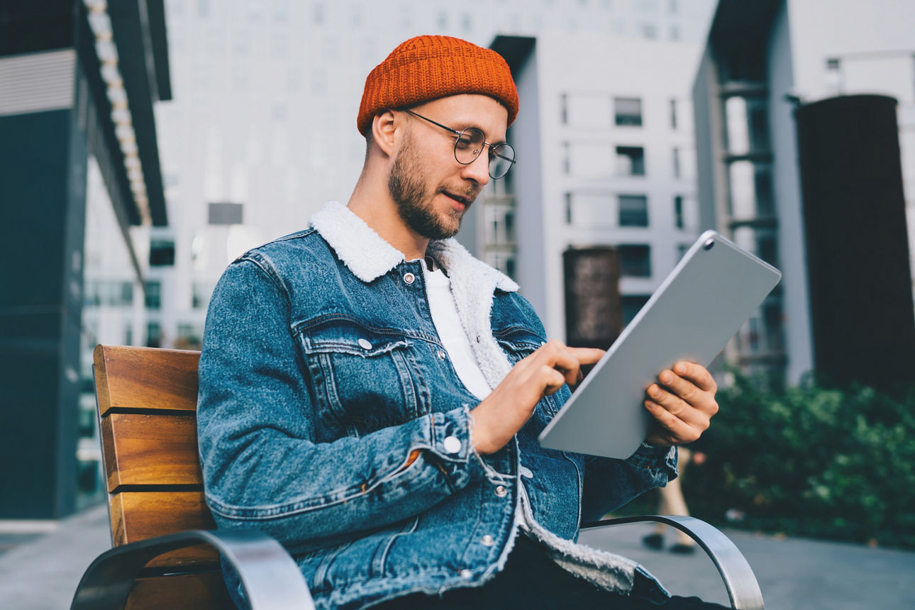 Ein Mann sitzt auf einer Bank und hält ein Tablet in der Hand